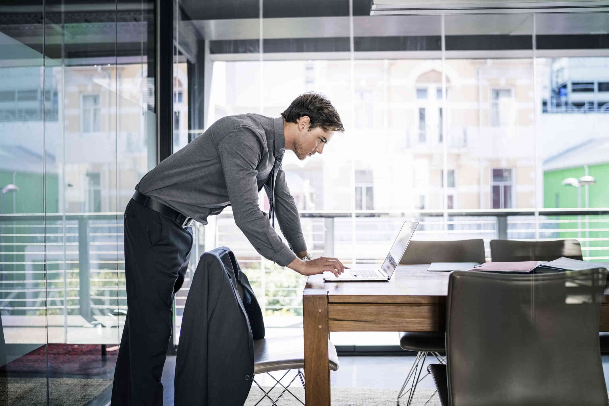 A man leaning closer to the table is busy scrolling on his laptop.