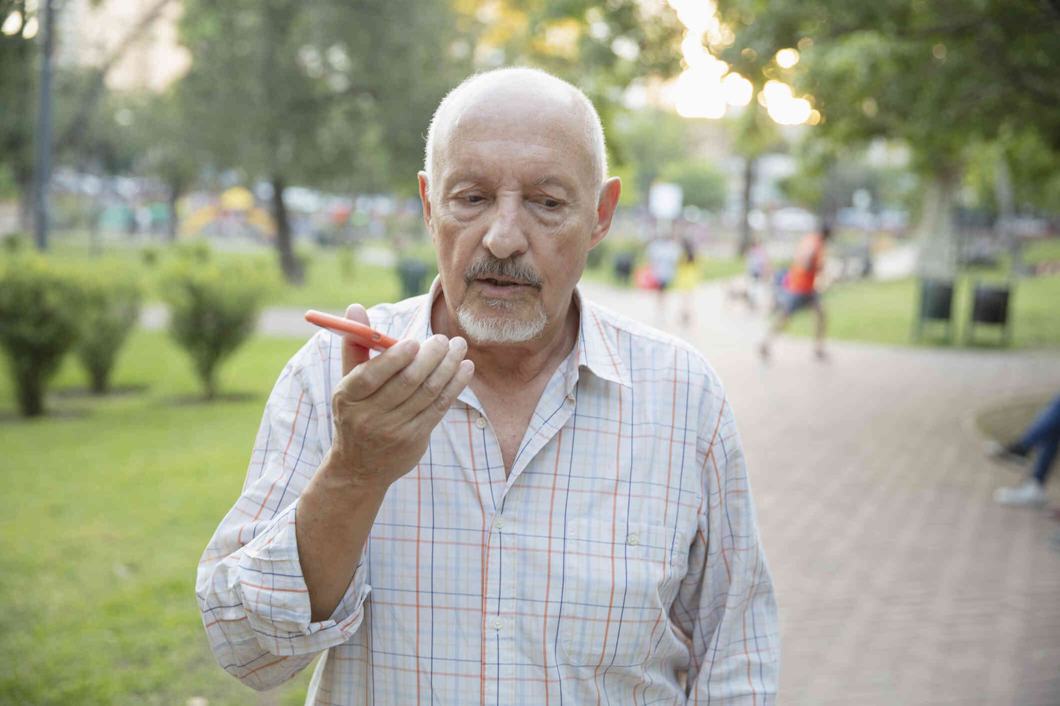 An elderly man standing outside is busy talking to someone over the phone.